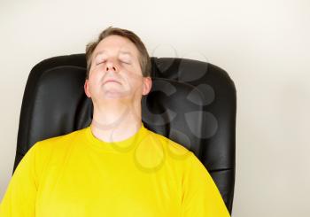 Horizontal photo of mature man relaxing in massage chair with eyes closed