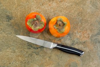 Horizontal photo of dry fresh persimmons with single knife lying on natural stone counter top 
