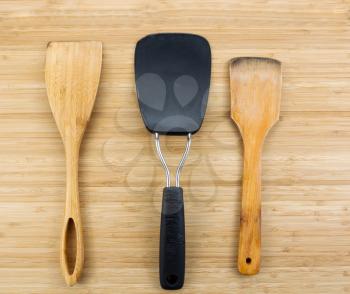 Photo of three kitchen spatulas, two of them wooden, on natural bamboo board
