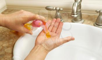 Horizontal photo of female hands putting liquid soap in palm of hand with bathroom sink in background 