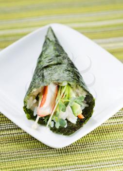 Closeup vertical photo of freshly handmade Temaki sushi cone in white plate with textured green cloth mat underneath 