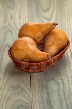 Vertical photo of three ripe pears in a small basket on faded wood