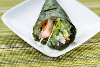 Closeup horizontal photo of freshly handmade Temaki sushi cone in white plate with textured cloth mat underneath 