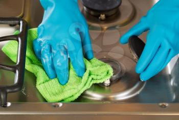 Closeup horizontal image of hands wearing rubber gloves while removing soap from stove top range green with microfiber rag

