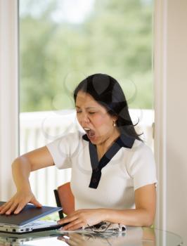 Vertical image of mature woman angrily slamming her laptop shut while working from home with blurred out daylight coming in from window in background