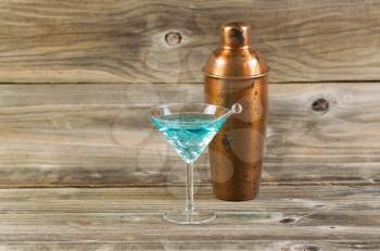 Horizontal photo of a mixed drink and a metal mixer resting on rustic wood