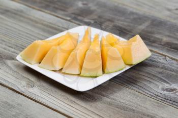 Closeup view of a freshly cut melon slices on white plate on rustic wood