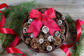 Overhead view of a basket filled with pine cones and large red bow for Christmas season on rustic wood 