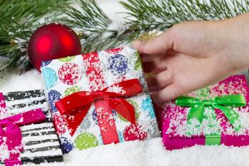 Closeup horizontal view of female hand picking up a holiday wrapped gift from the snow 