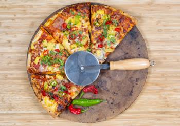 Top view of a freshly baked pizza with cutter on stone and natural bamboo board
