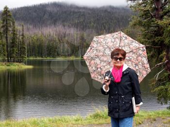 Image of senior women, holding umbrella, while near lake in Yellowstone National Park 