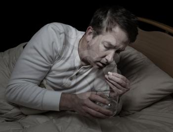 Horizontal image of sick mature man, taking medicine, while in bed 