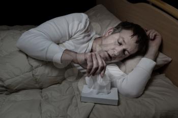 Horizontal image of sick mature man, reaching for tissue, while in bed 