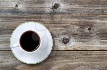 Overhead view of freshly brewed black coffee in white cup with saucer underneath on vintage wood 
