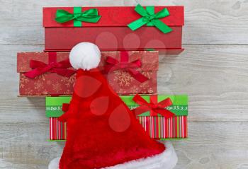 Top view of holiday gift wrapped boxes with Santa cap on rustic white wood 