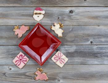 Top view of Christmas cookies surrounding red plate with rustic wood underneath