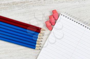 Pencil tips and erasers pointing at a blank spiral notepad on rustic white wood