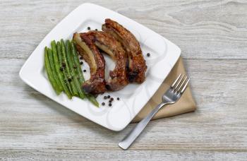 Close up of freshly cooked barbecued pork spare ribs, green beans on white plate with fork and cloth napkin 