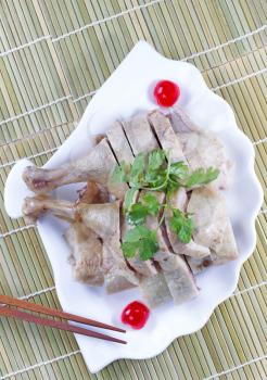 Vertical top view image of Chinese cooked chicken, parsley, cherry and chopsticks in shell shaped white plate with natural bamboo place mat background 