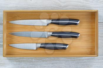 Close up horizontal image of a new wooden kitchen drawer with knife set resting on rustic white wood 