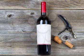 Top view angled shot of red wine bottle with corks and opener on rustic wooden boards