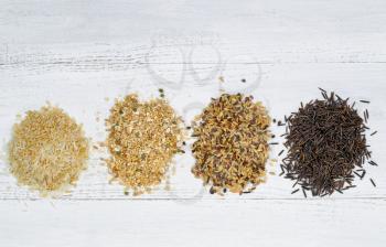 Top view of various rice types each within an individual pile on white wood