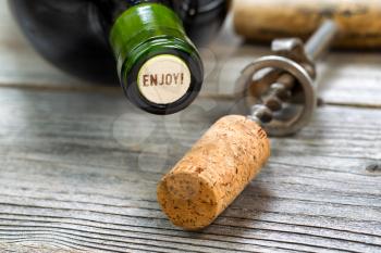 Close up shot of top of wine bottle cork, focus on the words enjoy, with rustic opener in background. Horizontal format layout. 