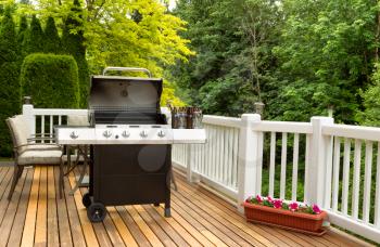 Photo of an open barbecue cooker with cold beer in bucket on cedar wooden patio. Table and colorful trees in background. 