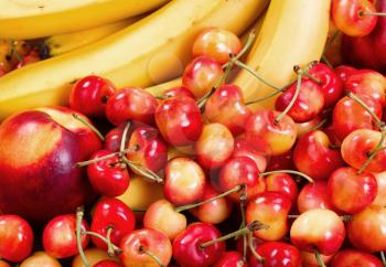Close up of a fresh pile of fruit consisting of cherries, peaches and bananas. Layout in filled frame format. 