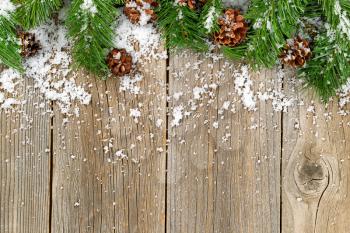 Christmas border with pine tree branches, cones and snow on rustic wooden boards. 