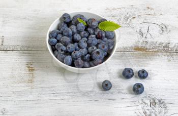 Close up of fresh blueberries, inside and outside of bowl, on rustic white wooden table. 