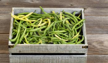 Old crate filled with freshly picked green and yellow beans on rustic wooden boards.