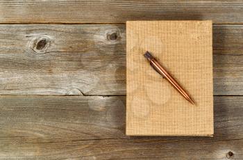 Vintage metal pen and burlap covered notepad on rustic wooden desktop.