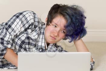 Unhappy teen girl looking at computer while listening to music at home. 