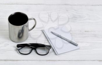 White desktop with coffee, pen, paper, and reading glasses. Layout in horizontal format.