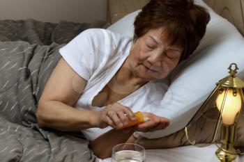 Close up of senior woman, taking medicine out of bottle, while in bed. Sick concept.