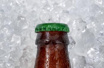 Close up of a single partial bottle of beer cap cooling down on pile of ice. Layout in horizontal format. 
