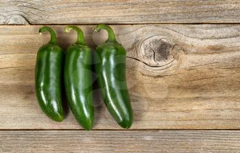 Three mature Jalapeno peppers, with rough texture, on rustic wood.