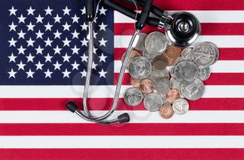United States of America flag with stethoscope and coin money. USA financial health concept. Overhead view in horizontal layout.