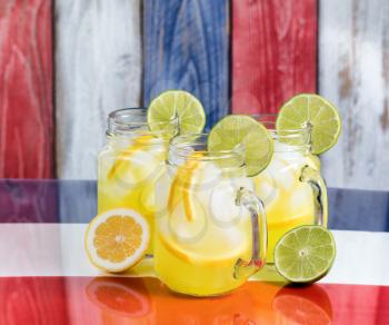 Front view of a glasses filled with cold lemonade.  Faded wooden boards painted red, white and blue in background.