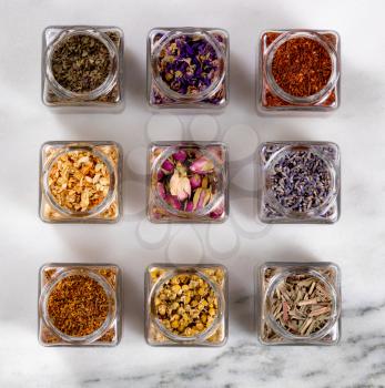 Overhead view of herbs and spices in glass jars on white marble stone.