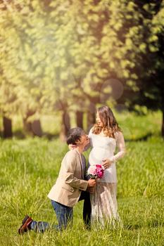 Future dad, with flowers, kneeling to expecting mom in open grassy field. Haze light effect applied to image.    