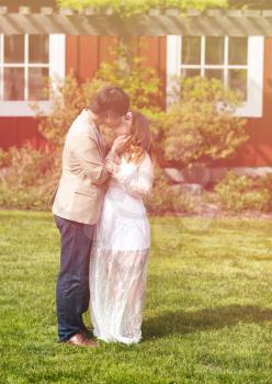Expecting mom and dad kissing each other while outdoors in warm light. Lighting effect applied to image. 
