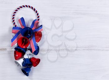 Colorful bells and ribbons on rustic white wooden boards. Fourth of July holiday concept for United States of America.  