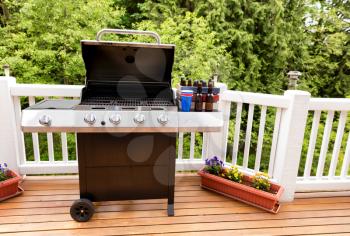 Open large barbecue cooker, bottled beer, cup, and crate on cedar wood deck with trees in background. 