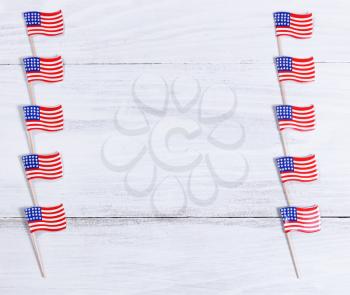 Small USA flags lined up on right and left sides of rustic white wooden boards. Fourth of July holiday concept for United States of America.  