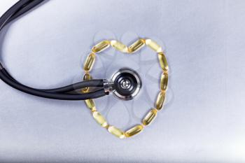 Healthy heart concept with fish oil capsules and stethoscope on stainless steel. 