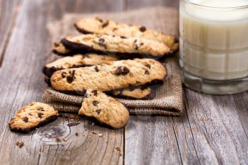 Close up of chocolate chip cookies in linen napkin with milk on rustic wood. Selective focus on broken cookies in forefront of image.