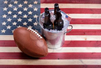 Top view of American football and bucket of ice cold beer on rustic wooden boards with painted USA Flag.