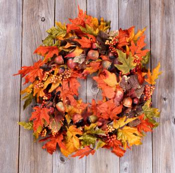 Overhead view of autumn wreath made with artificial leaves and acorns on rustic wood. 